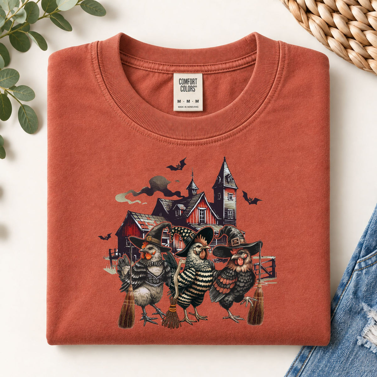 Rust-orange sweatshirt flat lay with witchy chicken and spooky house front graphic