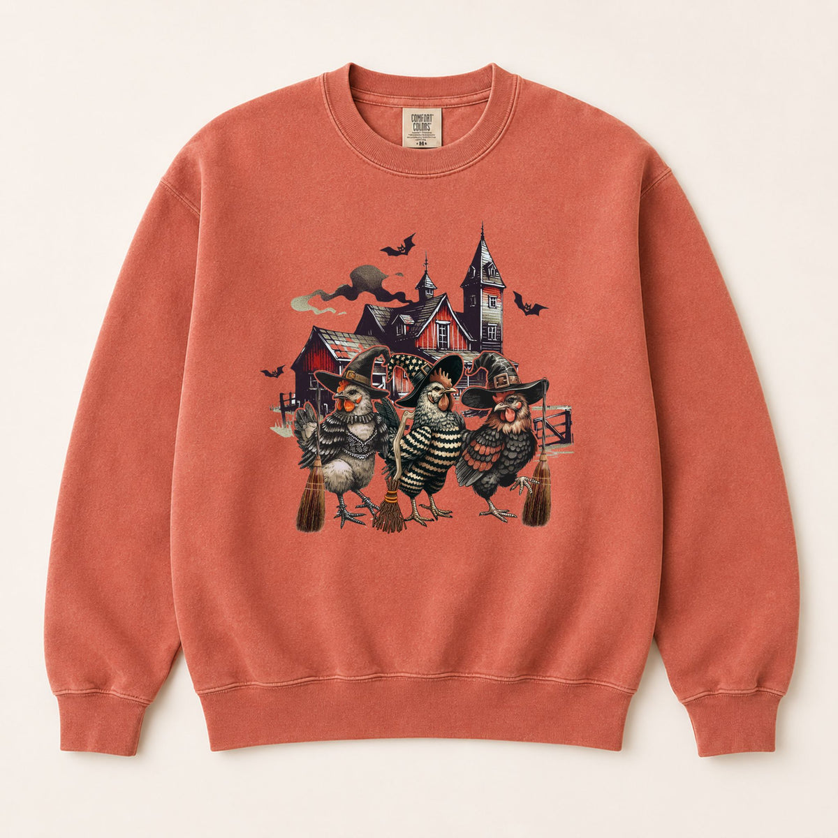 Rust-orange sweatshirt with witchy chicken and spooky house graphic, crewneck front