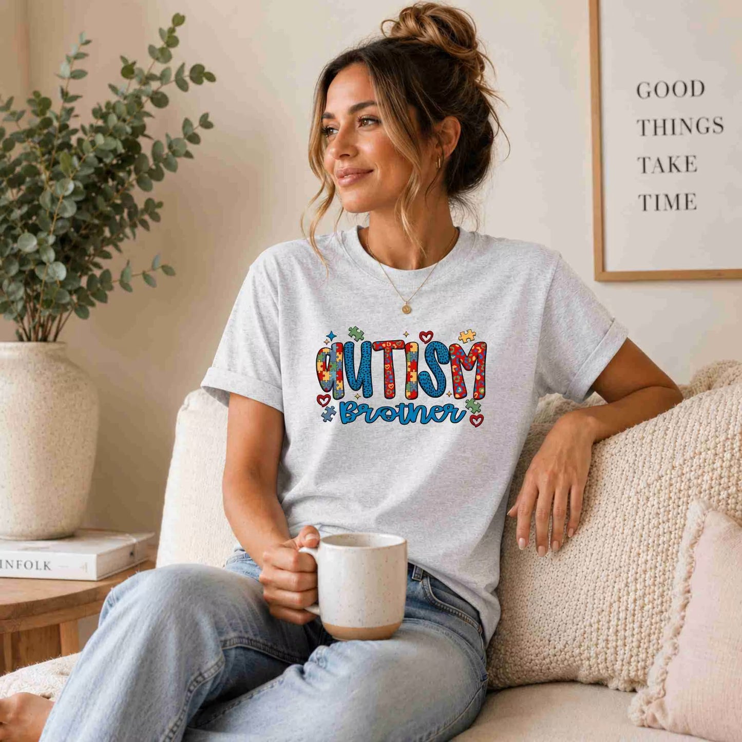 Woman wearing a 'Autism Brother' t-shirt, sitting on a couch holding a mug.