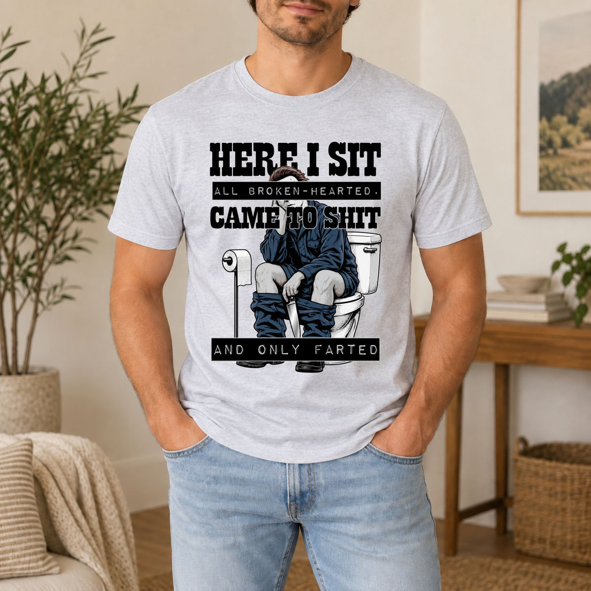 Light gray graphic tee with “HERE I SIT” horror-style toilet gag print on front.