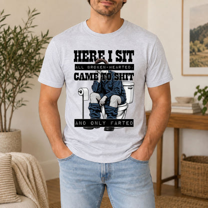 Light gray graphic tee with “HERE I SIT” horror-style toilet gag print on front.