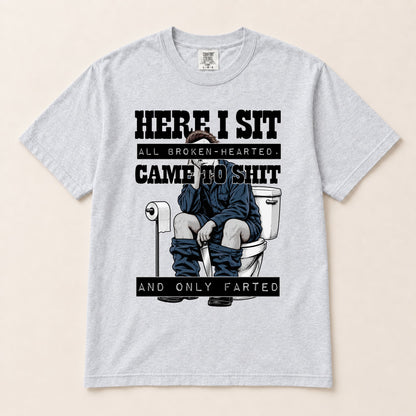 Light gray graphic short-sleeve tee with “HERE I SIT” toilet gag illustration centered.