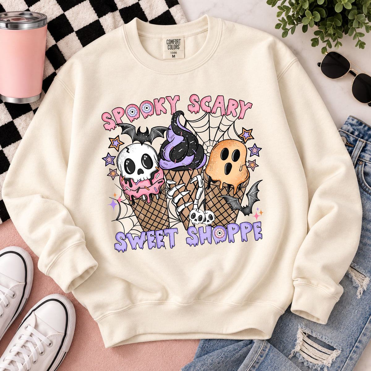Cream Halloween sweatshirt laid flat with skull, web, and ice-cream graphic