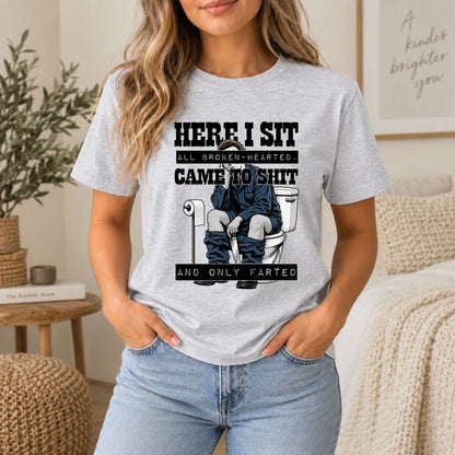 Light gray crewneck graphic t-shirt with toilet gag print and “HERE I SIT” text.