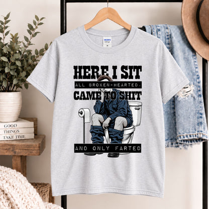 Light gray t-shirt on hanger featuring “HERE I SIT” toilet gag illustration on front.