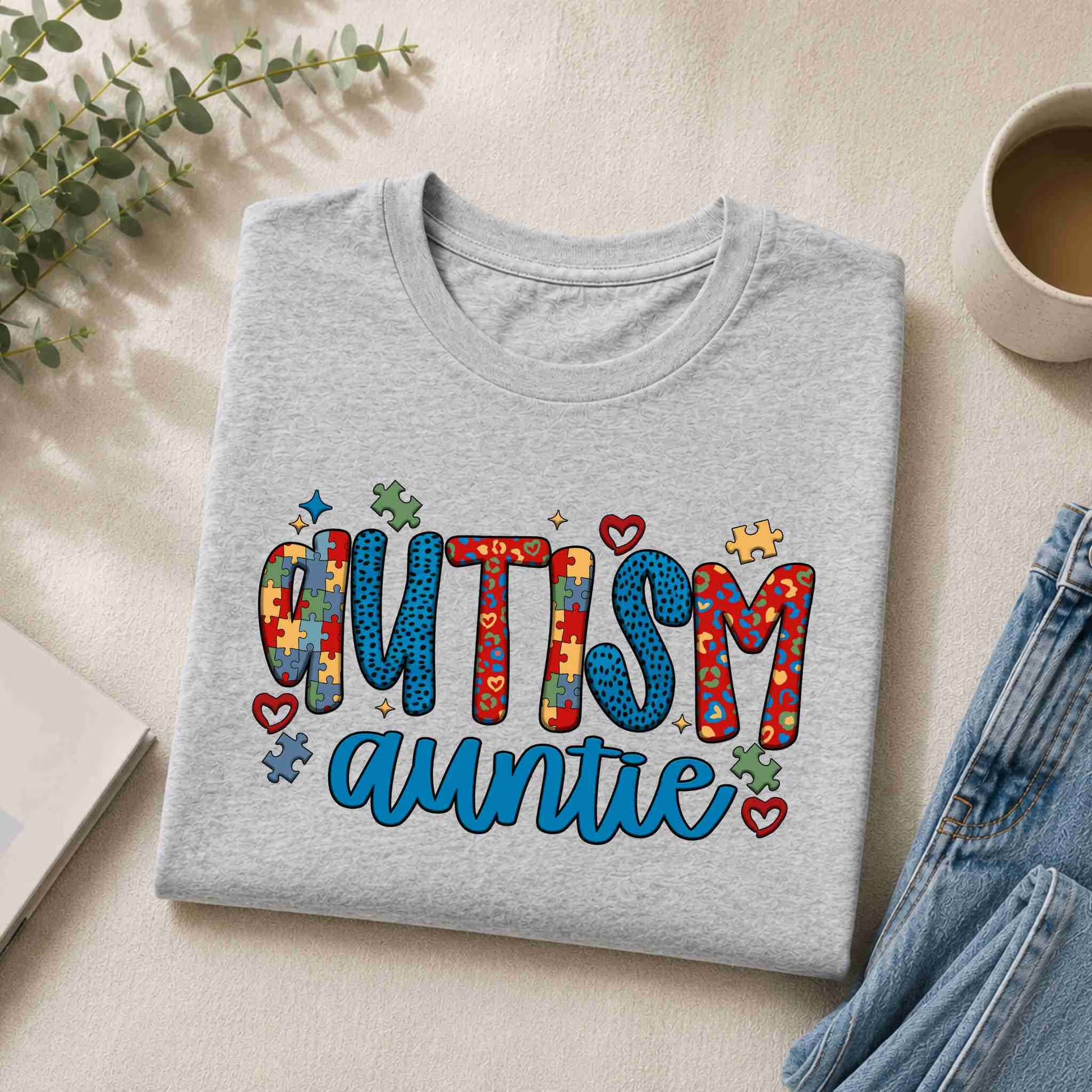 Gray sweatshirt with 'Autism Auntie' text on a light surface with a cup and plant.