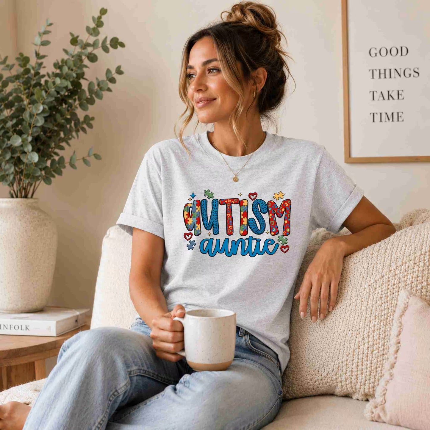 Woman wearing a 'Autism Auntie' t-shirt, sitting on a couch holding a mug.