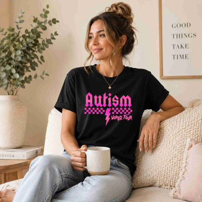 Woman wearing a black t-shirt with 'Autism World Tour' design, sitting on a couch holding a mug.