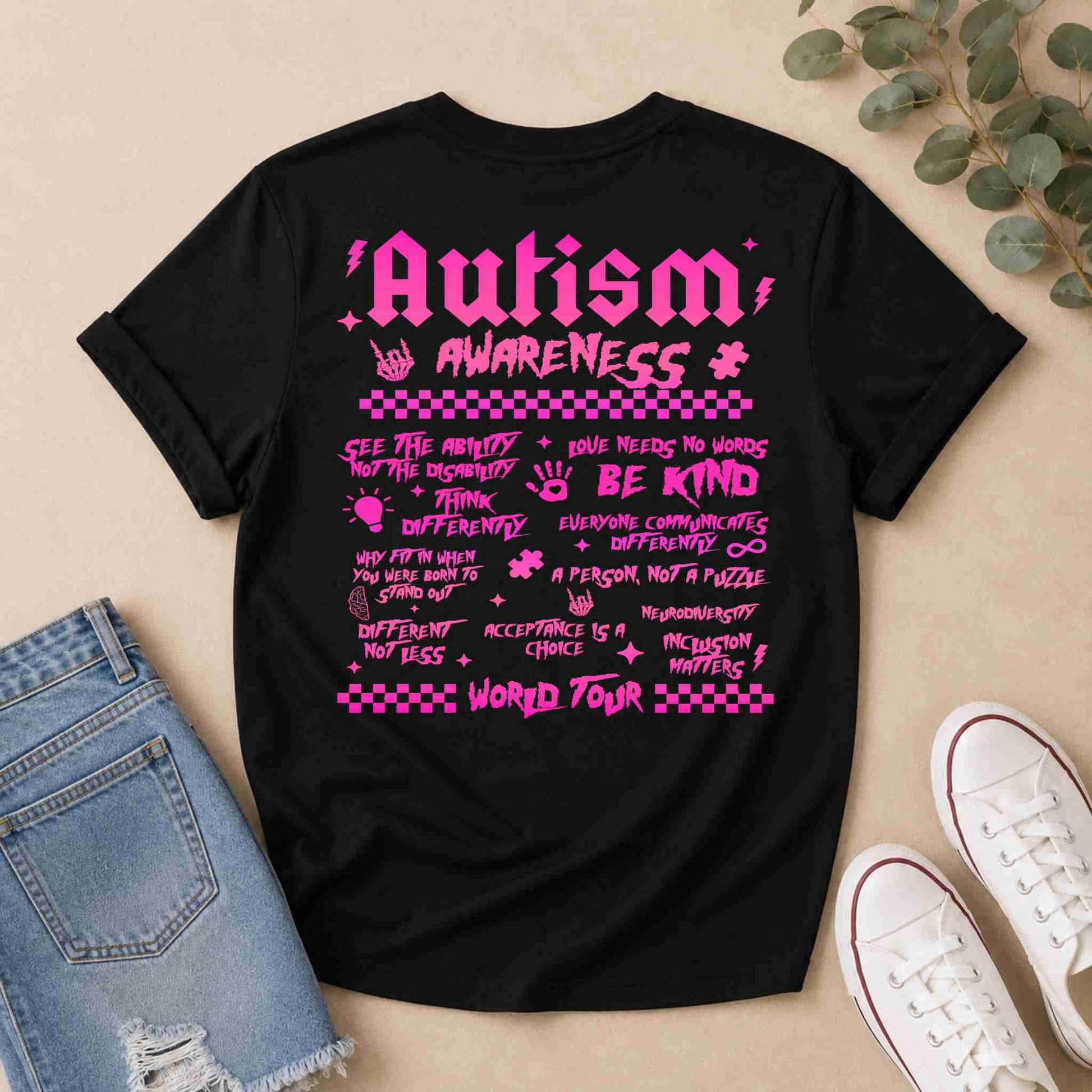 Black t-shirt with pink 'Autism World Tour' design on a light surface with casual items.