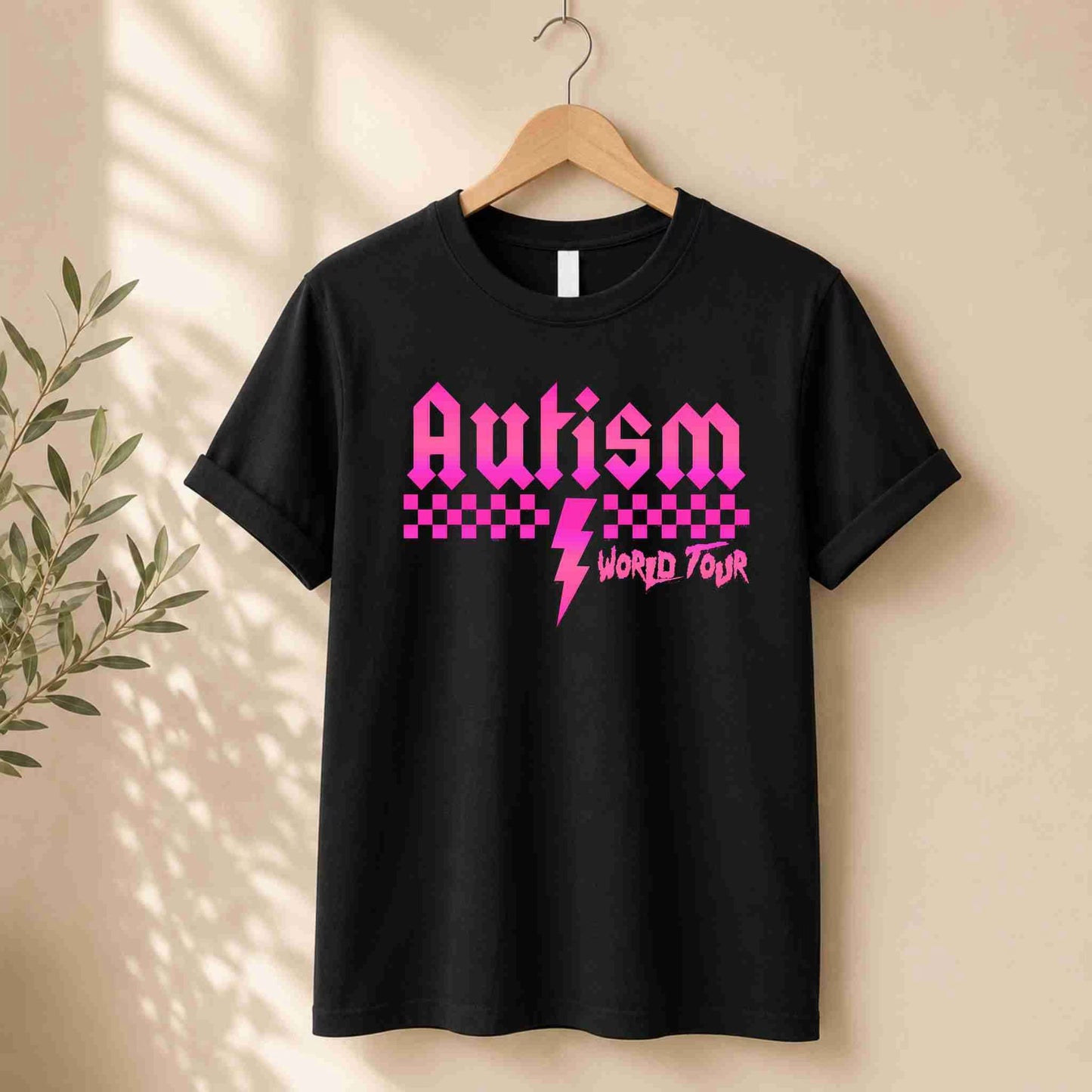 Black t-shirt with pink 'Autism World Tour' design on a light surface with casual items.