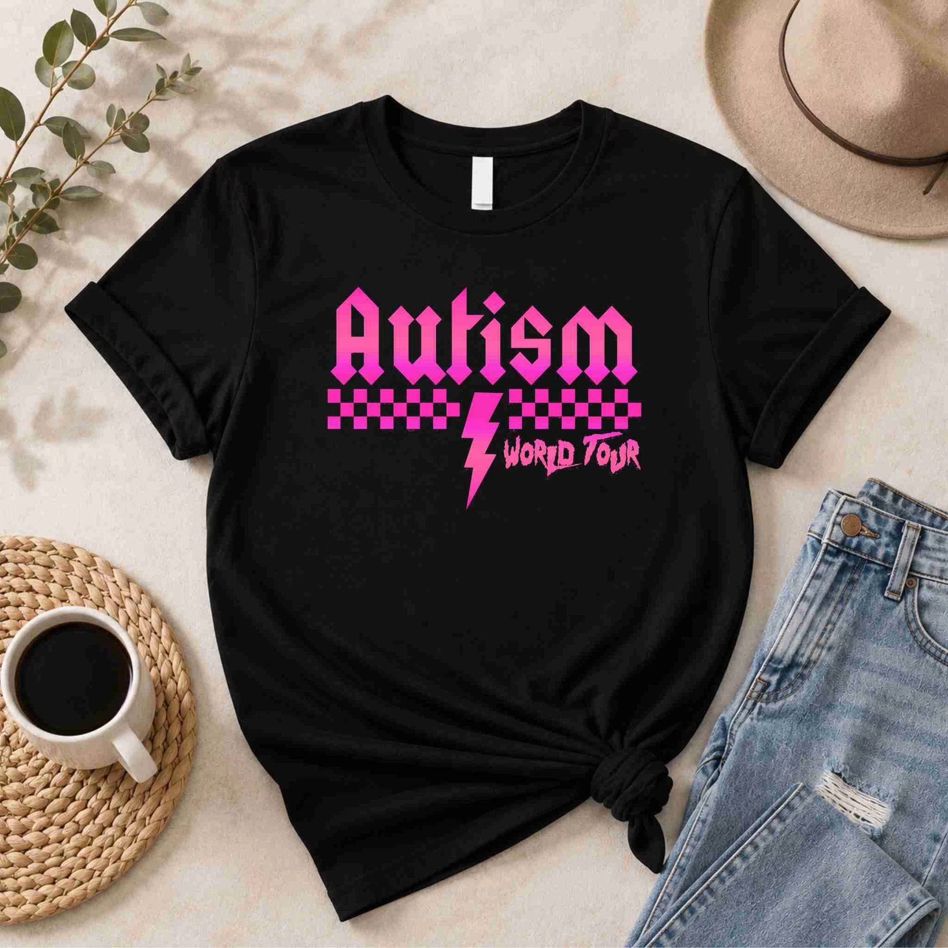 Black t-shirt with pink 'Autism World Tour' design on a light surface with casual items.