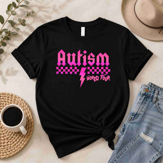 Black t-shirt with pink 'Autism World Tour' design on a light surface with casual items.