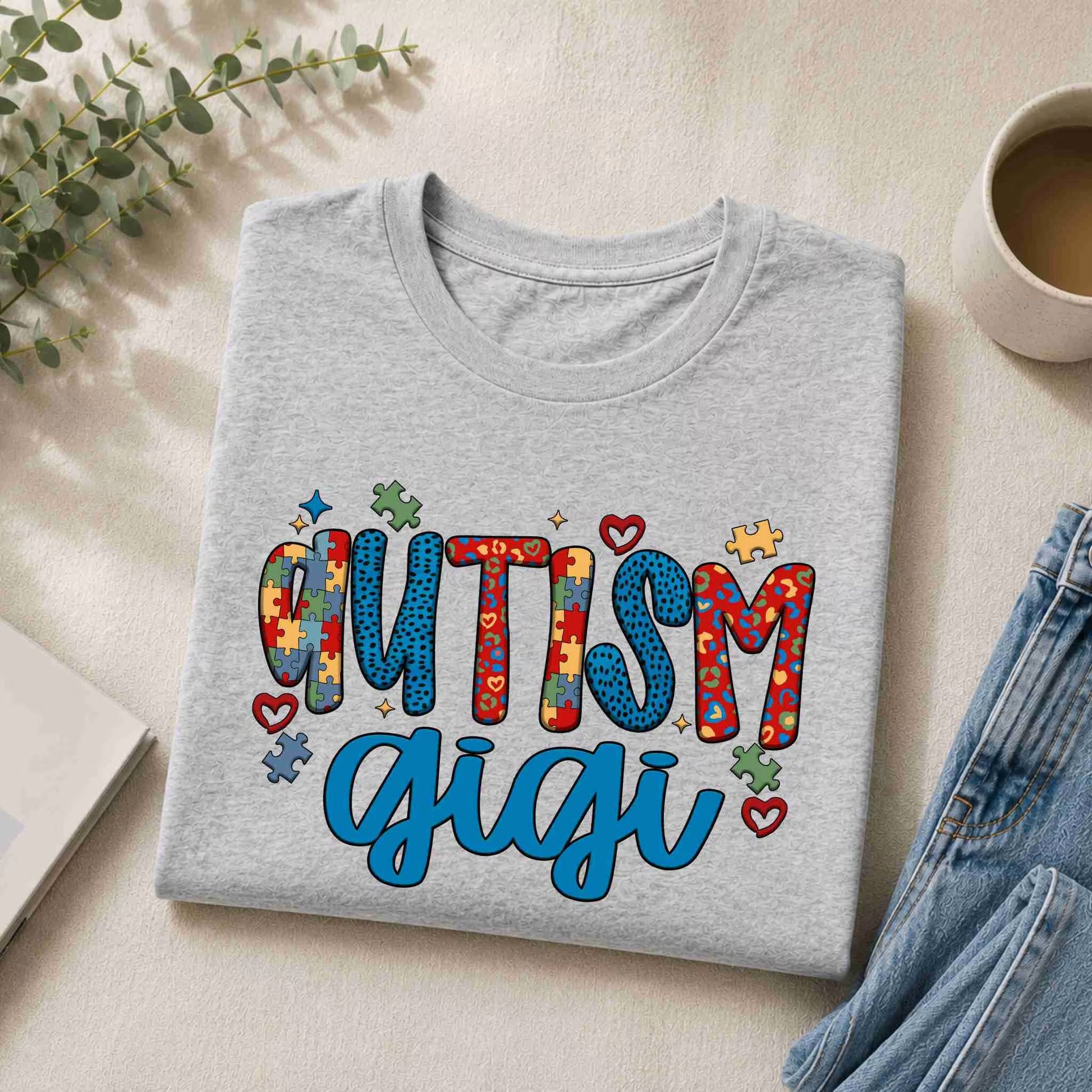 Gray sweatshirt with 'Autism Gigi' text on a light surface with a cup and plant.