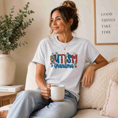Woman wearing a 'Autism Grandma' t-shirt, sitting on a couch holding a mug.