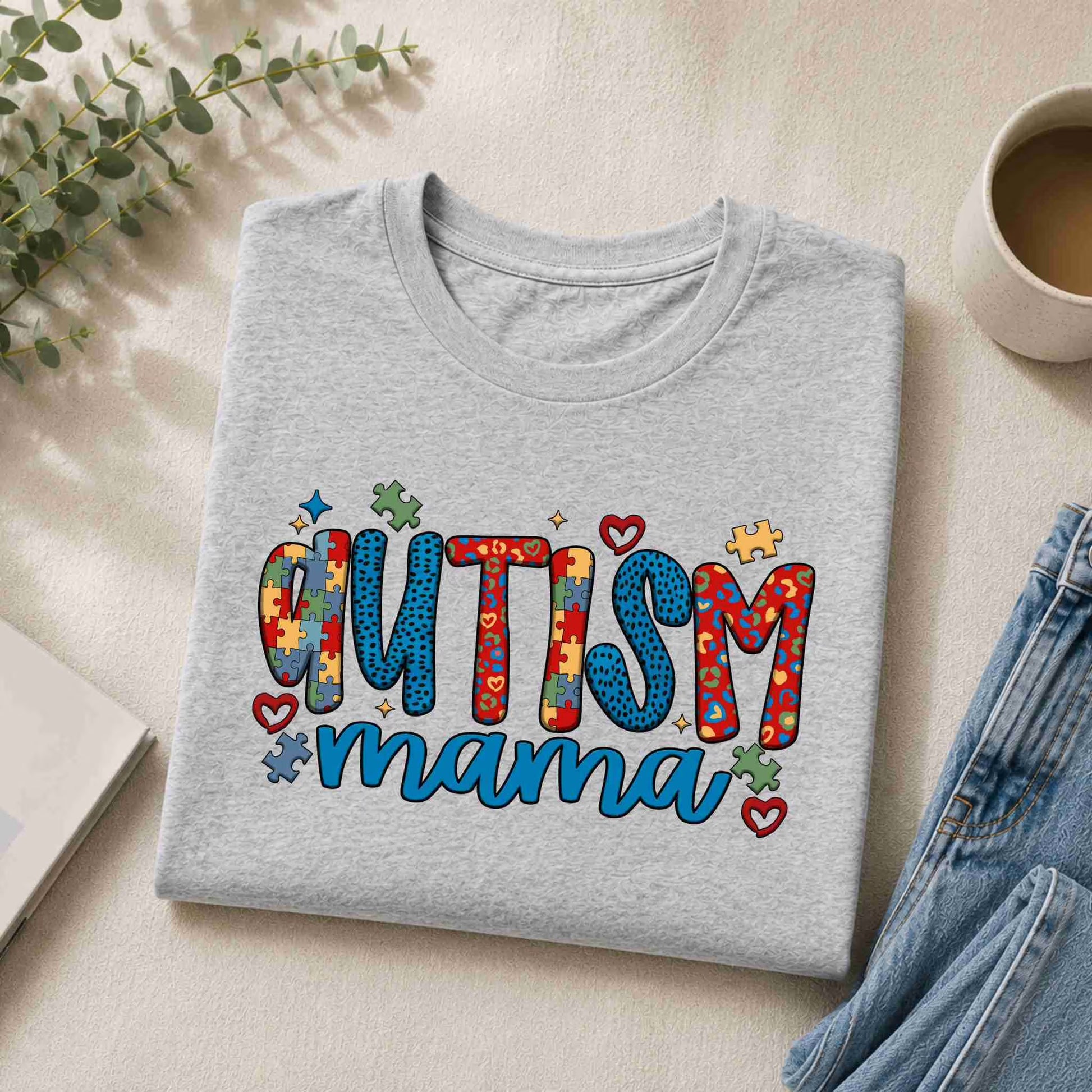 Gray sweatshirt with 'Autism Mama' text on a light surface with a cup and plant.
