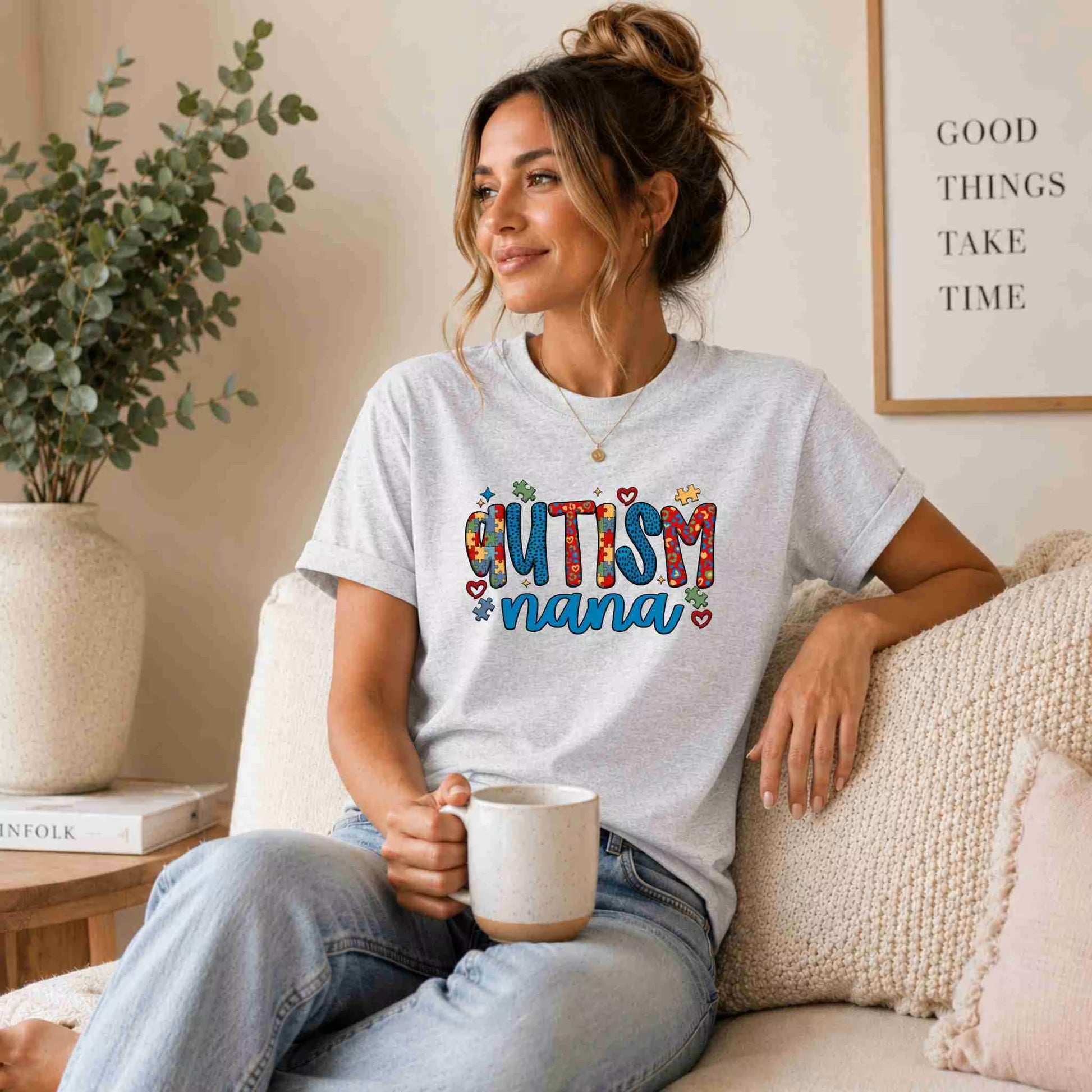 Woman wearing a 'Autism Nana' t-shirt, sitting on a couch holding a mug.