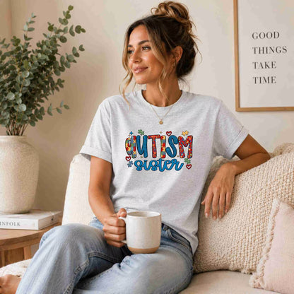 Woman wearing a 'Autism Sister' t-shirt, sitting on a couch holding a mug.