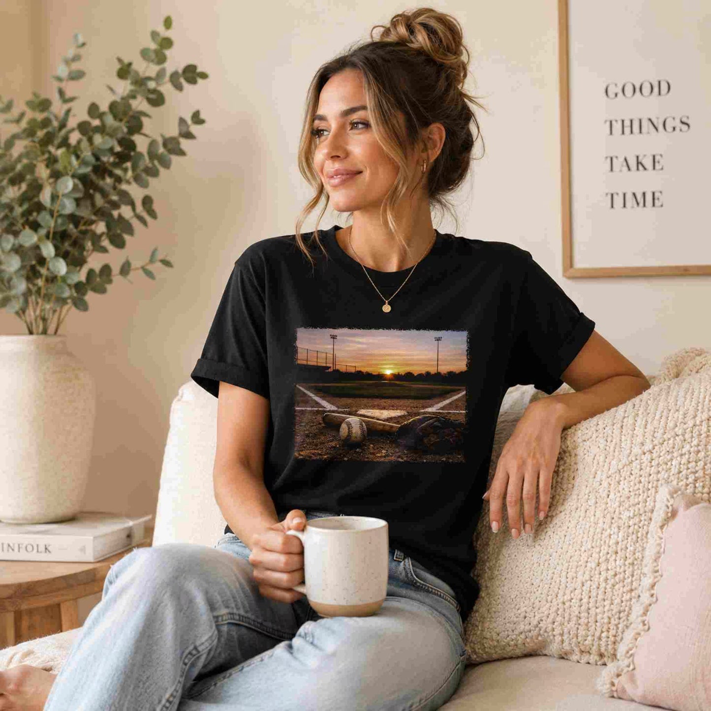 Woman wearing a black t-shirt with a scenic print, sitting on a couch holding a mug.