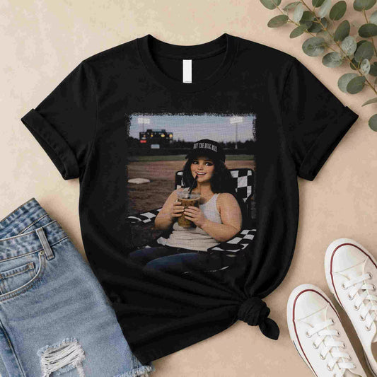 The Softball Mom Iced Coffee Bleacher Queen Graphic Tee by Becca's Banging Designs LLC features a smiling woman outdoors with a drink—a fun, trendy choice for softball moms and fans of women’s graphic t-shirts.