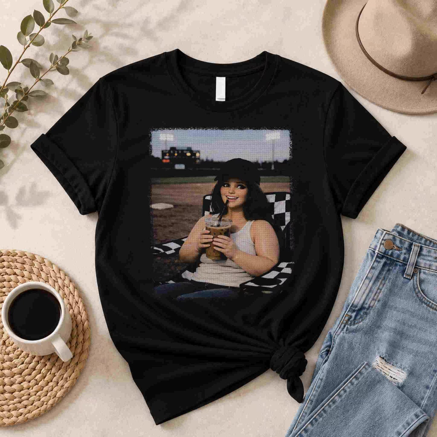 The Softball Mom Iced Coffee Bleacher Queen Graphic Tee by Becca's Banging Designs LLC is a trendy women’s shirt featuring a smiling woman outdoors with a drink—perfect for fans of affordable, fun graphic tees.