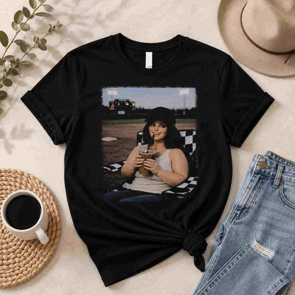 The Softball Mom Iced Coffee Bleacher Queen Graphic Tee by Becca's Banging Designs LLC is a trendy women’s shirt featuring a smiling woman outdoors with a drink—perfect for fans of affordable, fun graphic tees.