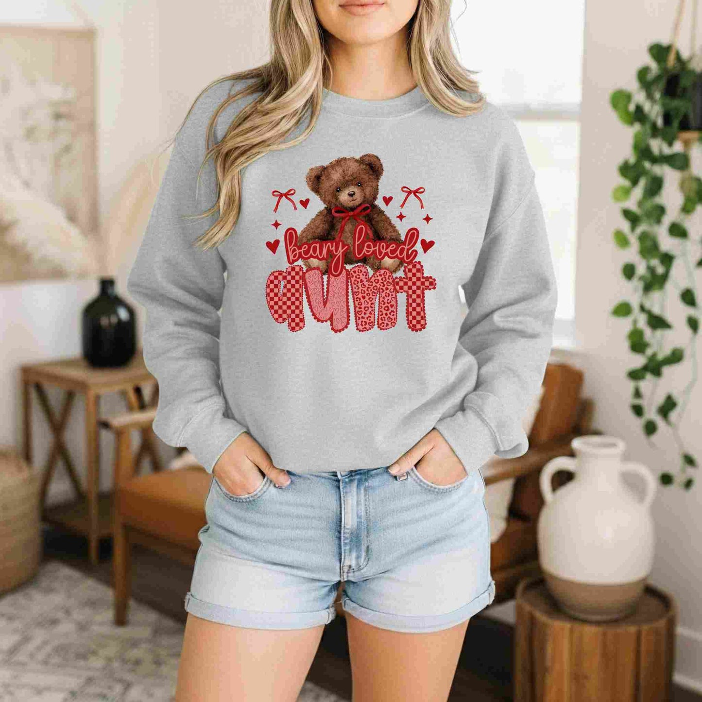 Person wearing a gray sweatshirt with a teddy bear graphic and 'bearly loved cum' text in a home setting.