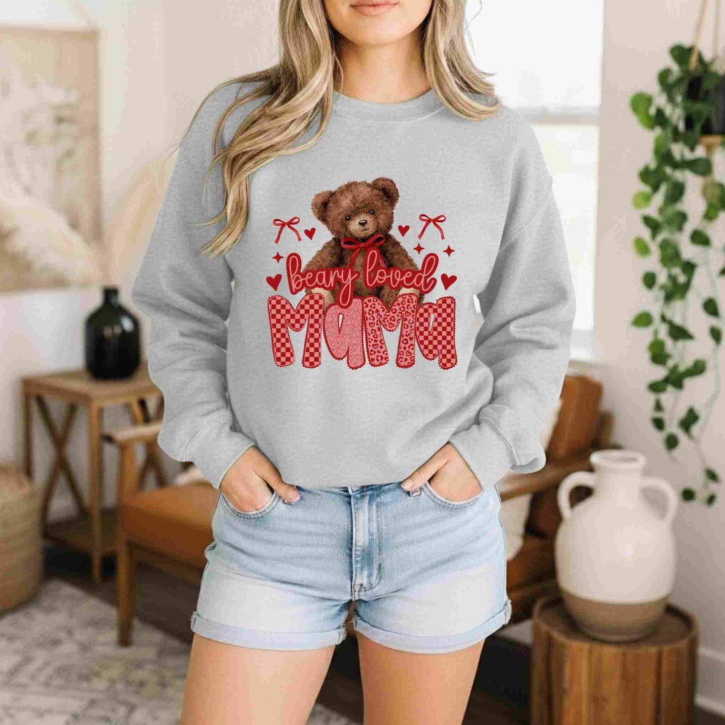 Person wearing a gray sweatshirt with a teddy bear graphic and 'bearly loved mom' text in a home setting.
