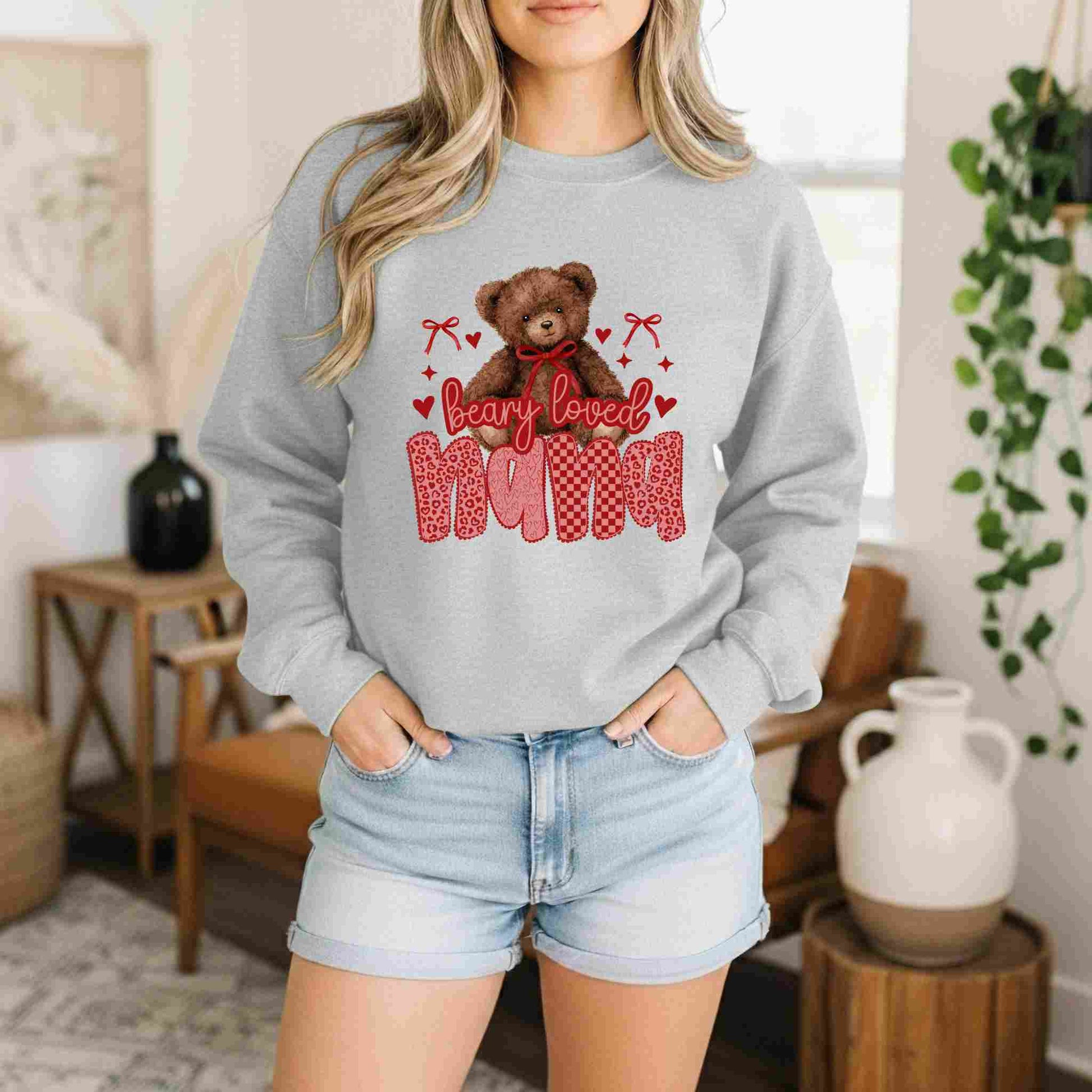 Person wearing a gray sweatshirt with a teddy bear graphic and 'bearly loved mom' text in a home setting.
