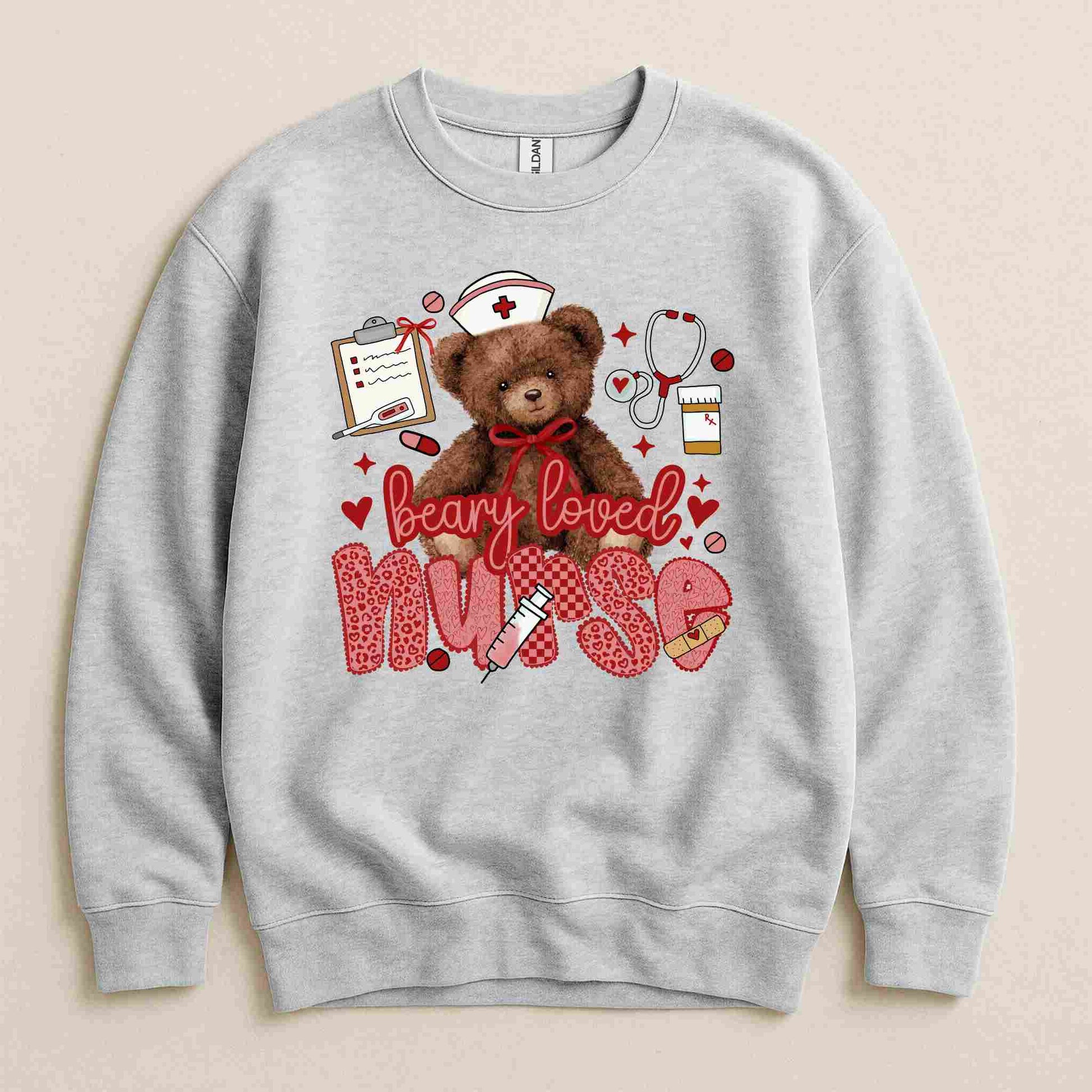 Becca's Banging Designs' Beary Loved Nurse Sweatshirt features a cute teddy bear in a nurse hat, surrounded by medical items and hearts—“Beary loved nurse” appears in red and pink. A cozy, thoughtful gift for nurses!.