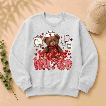The Beary Loved Nurse Sweatshirt Comfort Style and Care by Becca's Banging Designs features a cute teddy bear in a nurse hat with medical items and hearts, plus playful "beary loved nurse" text—an ideal gift for nurses.
