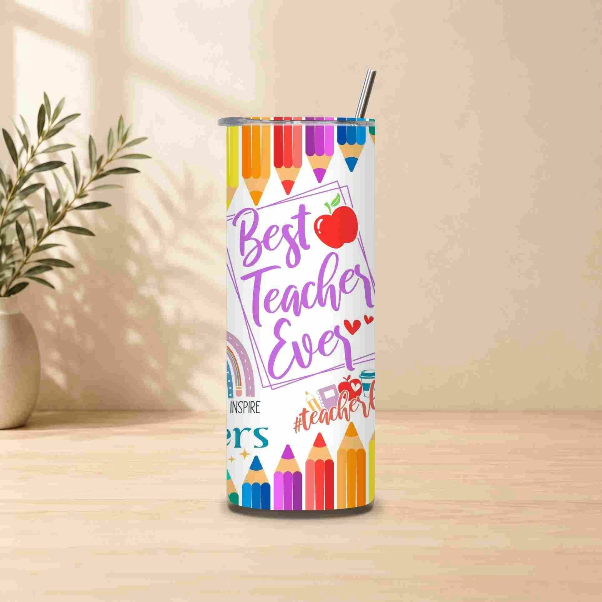The Best Teacher Ever | 20oz Tumbler, featuring playful pencils and rainbows, sits on a wooden table with a straw—a perfect teacher gift. A potted plant is visible in the background.