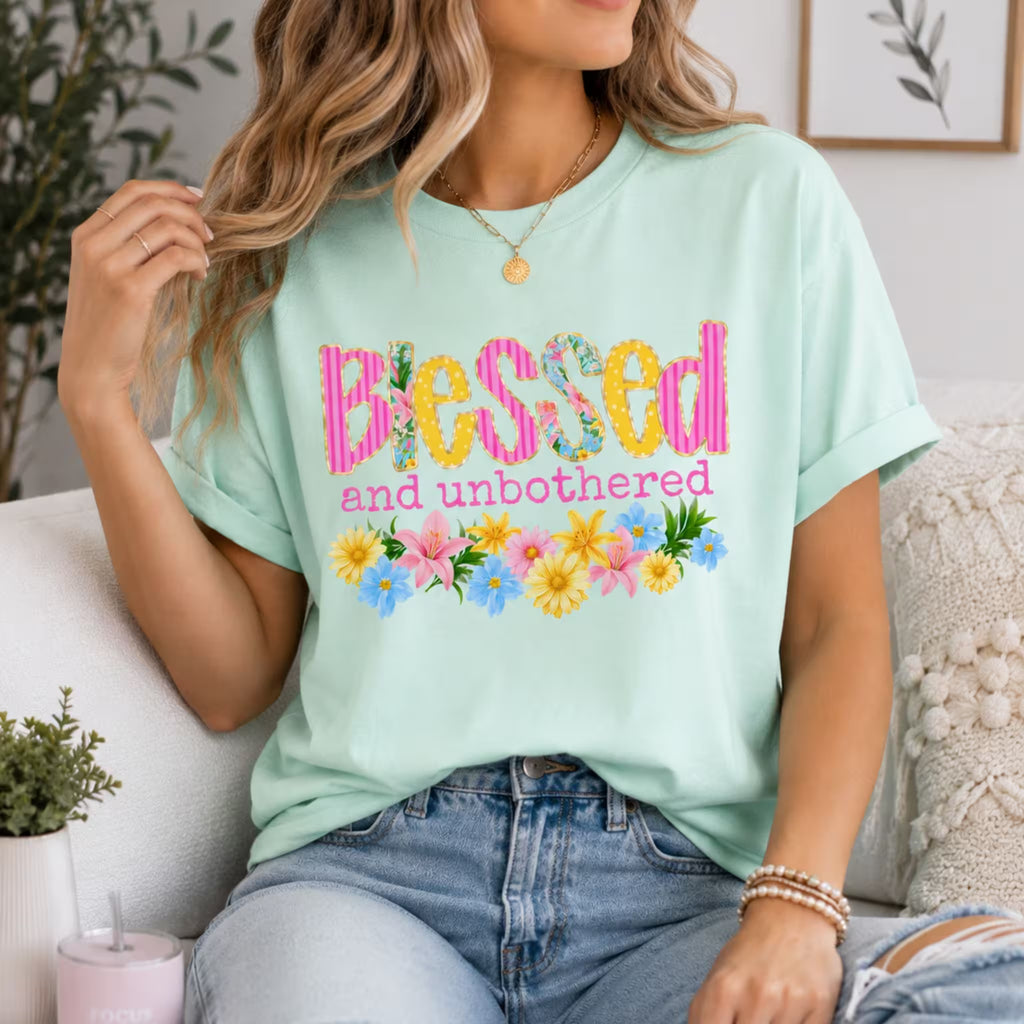 Person wearing a light green t-shirt with 'Blessed and unbothered' text and floral designs, sitting on a couch.