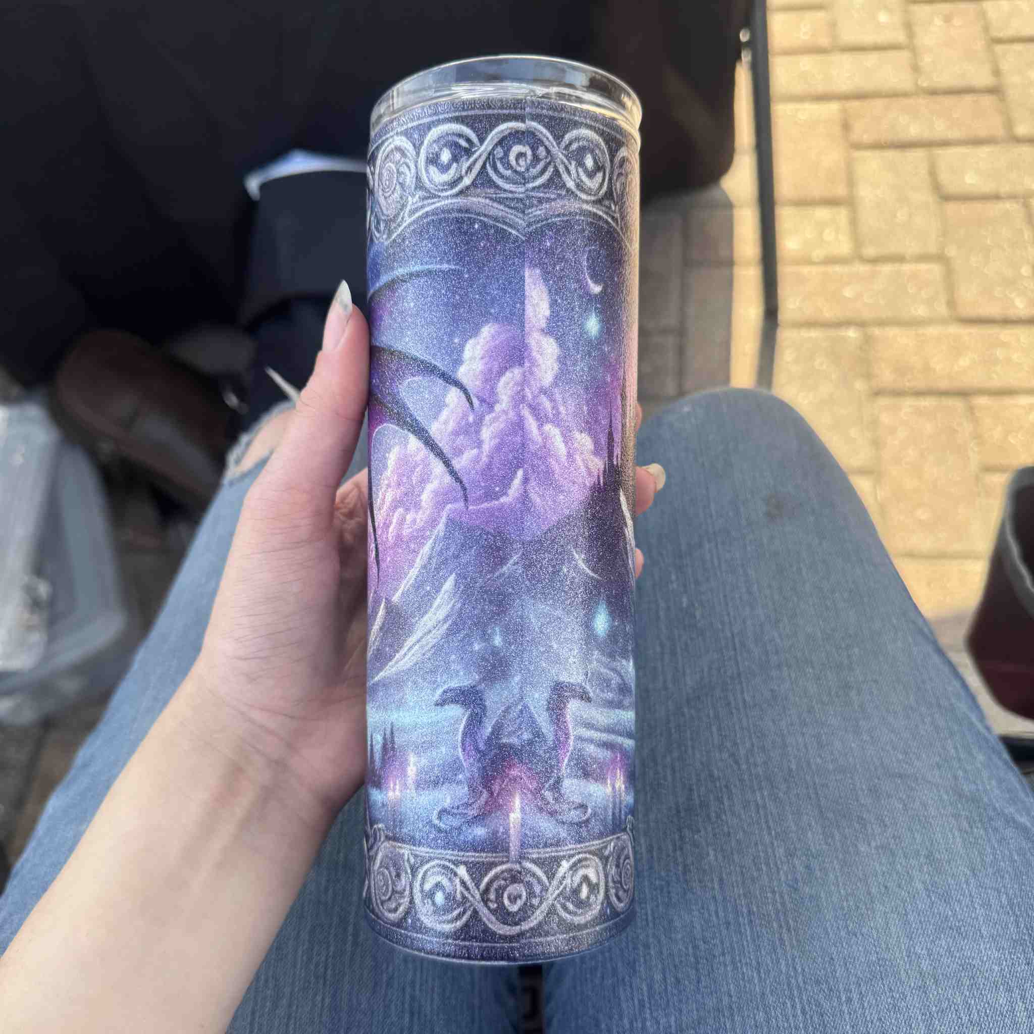 Tumbler with fantasy design held by a person outdoors.