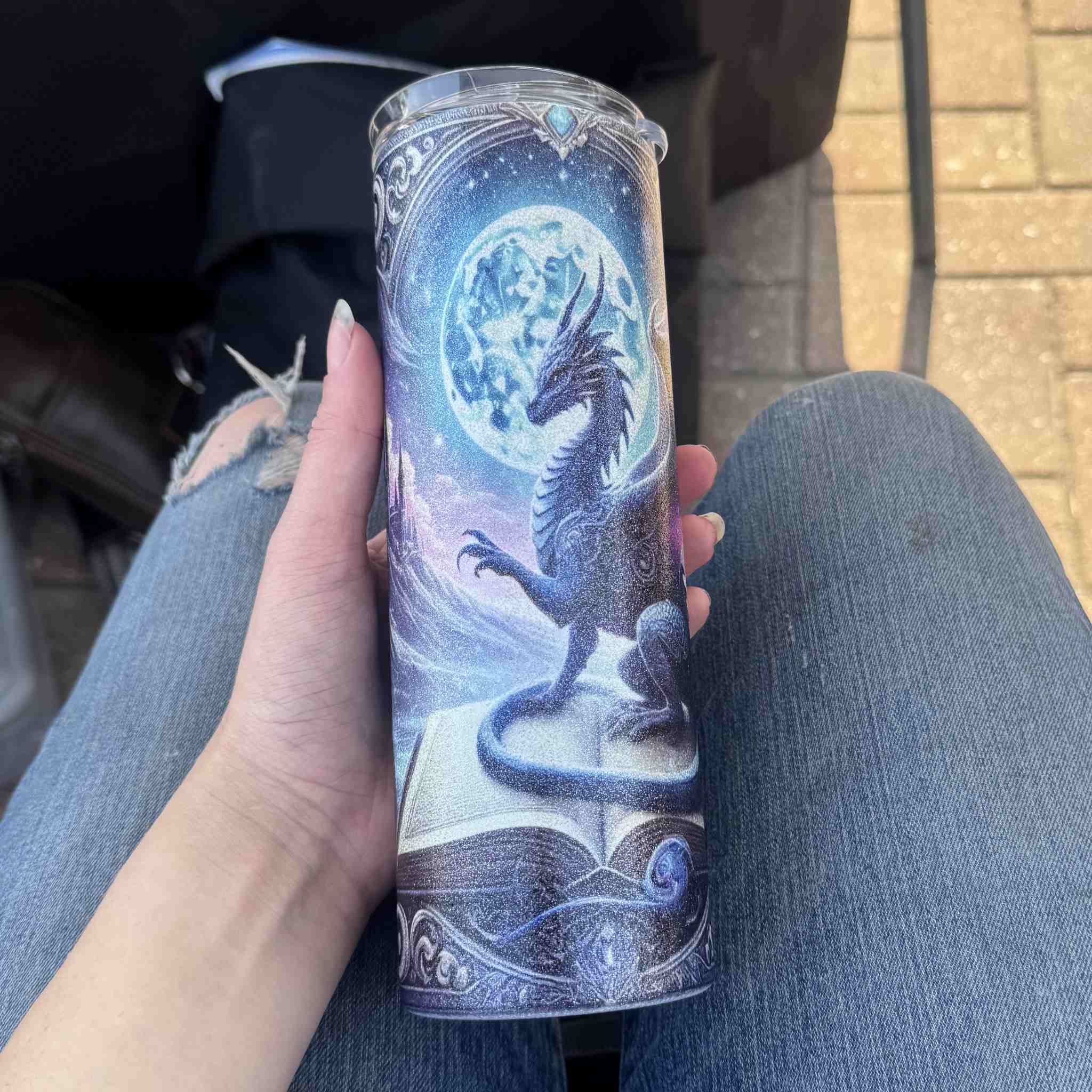 Person holding a tumbler product with dragon design against a blurred background