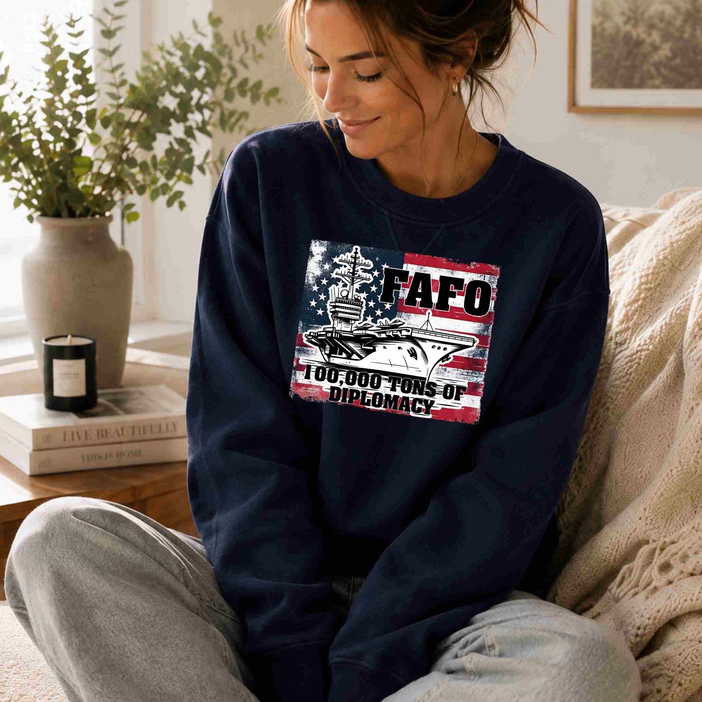 Woman wearing a navy sweatshirt with a graphic design, sitting on a couch in a cozy living room.