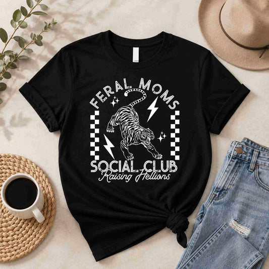 The Feral Moms Social Club Shirt – Raising Hellions Graphic Tee from Becca's Banging Designs LLC showcases a roaring tiger, lightning bolts, and checkerboard graphic—perfect to pair with jeans and coffee for bold everyday style.