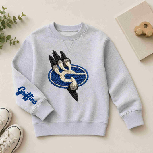 The Gateway Griffins | Crewneck by Becca’s Banging Designs is an oversized light gray sweatshirt with a textured embroidered paw print and blue oval front, "Griffins" on the sleeve, styled with white sneakers, a plant, and wooden toy.