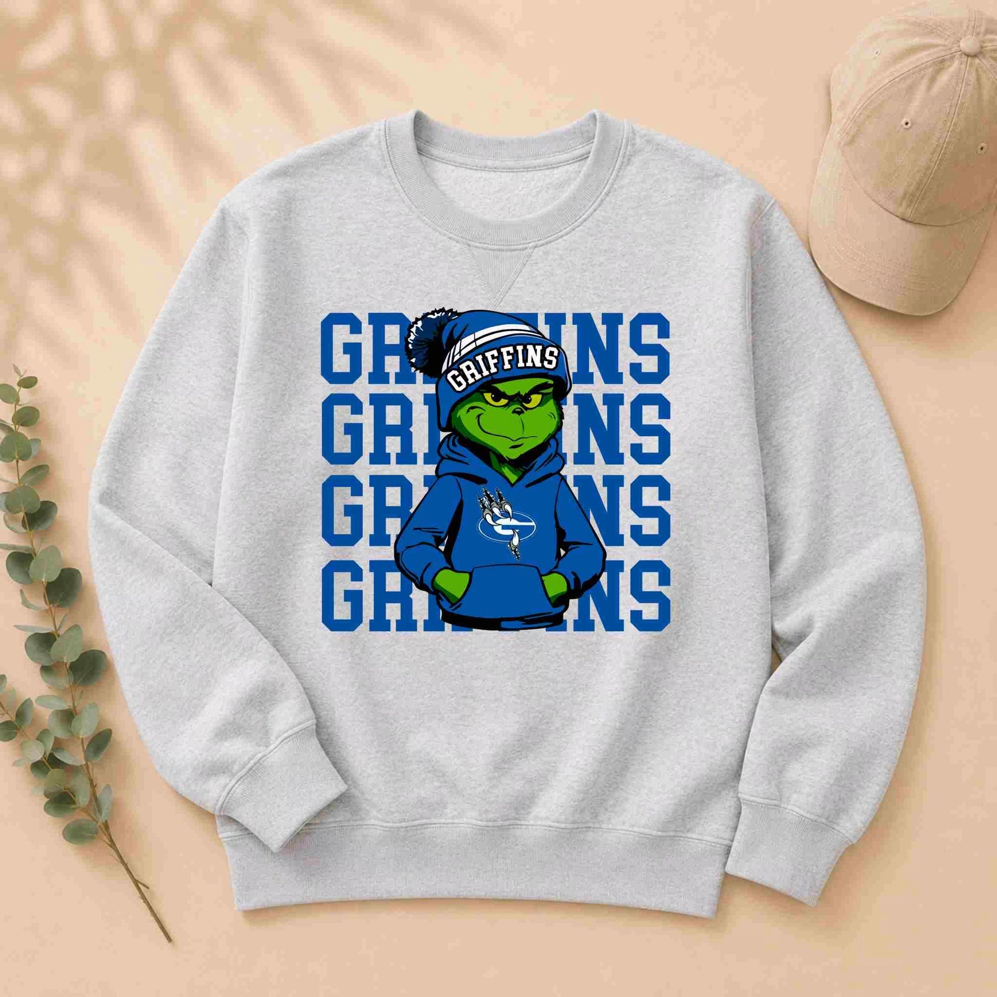 The Griffins Crewneck Sweatshirt Youth Comfort and Style by Becca's Banging Designs features a gray youth sweatshirt with a cartoon Grinch in blue Griffins gear and bold "GRIFFINS" print—perfect for showing school spirit.