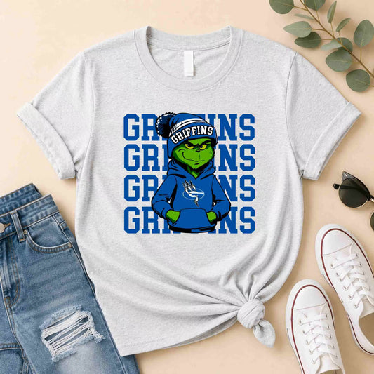 The Griffins Graphic Tee Youth Comfort and School Spirit by Becca's Banging Designs features a green creature in a blue hoodie and winter hat before bold GRIFFINS lettering—perfect for school spirit and comfort with your favorite jeans.