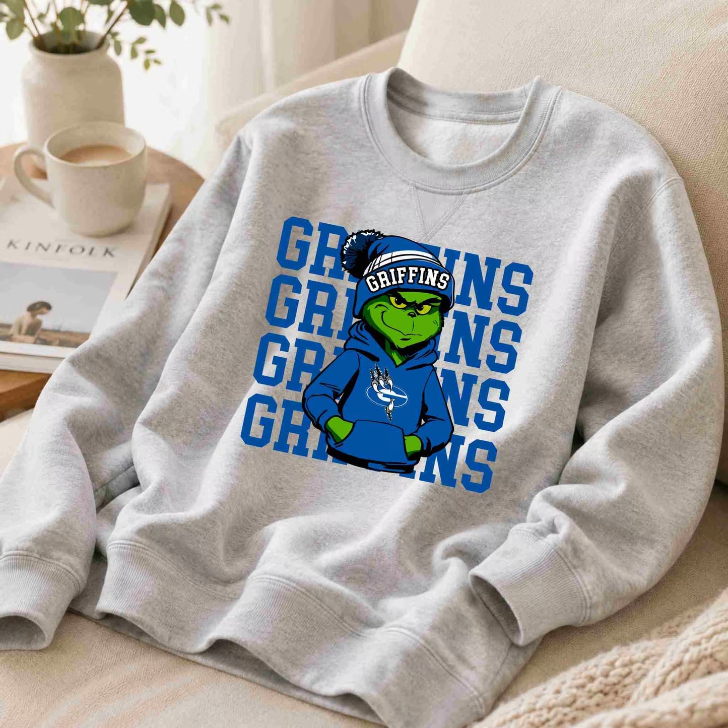 The Griffins Crewneck Sweatshirt Youth Comfort and Style by Becca's Banging Designs features a gray design with a green illustrated character in a blue hoodie and beanie, plus bold GRIFFINS text—ideal for showing off your school spirit.