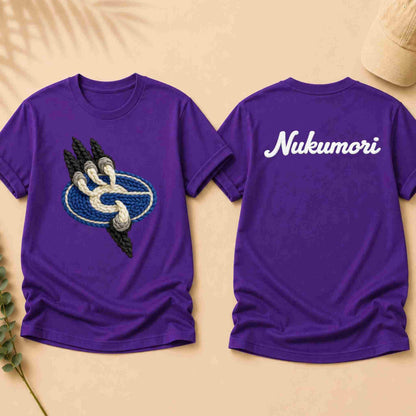 Purple t-shirt with a graphic design on the front and 'Nukumori' text on the back, displayed on a beige surface.