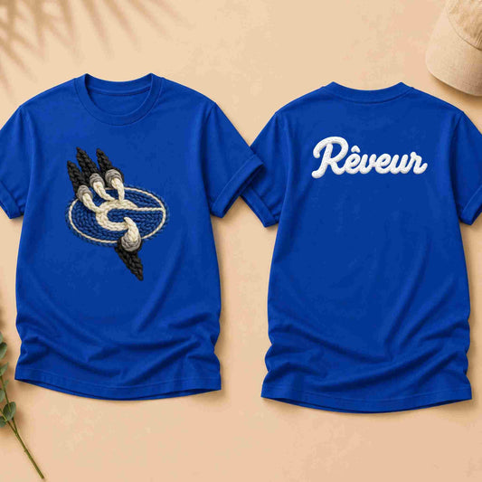 Blue t-shirt with a graphic design on the front and 'Rèveur' text on the back, displayed on a beige surface.