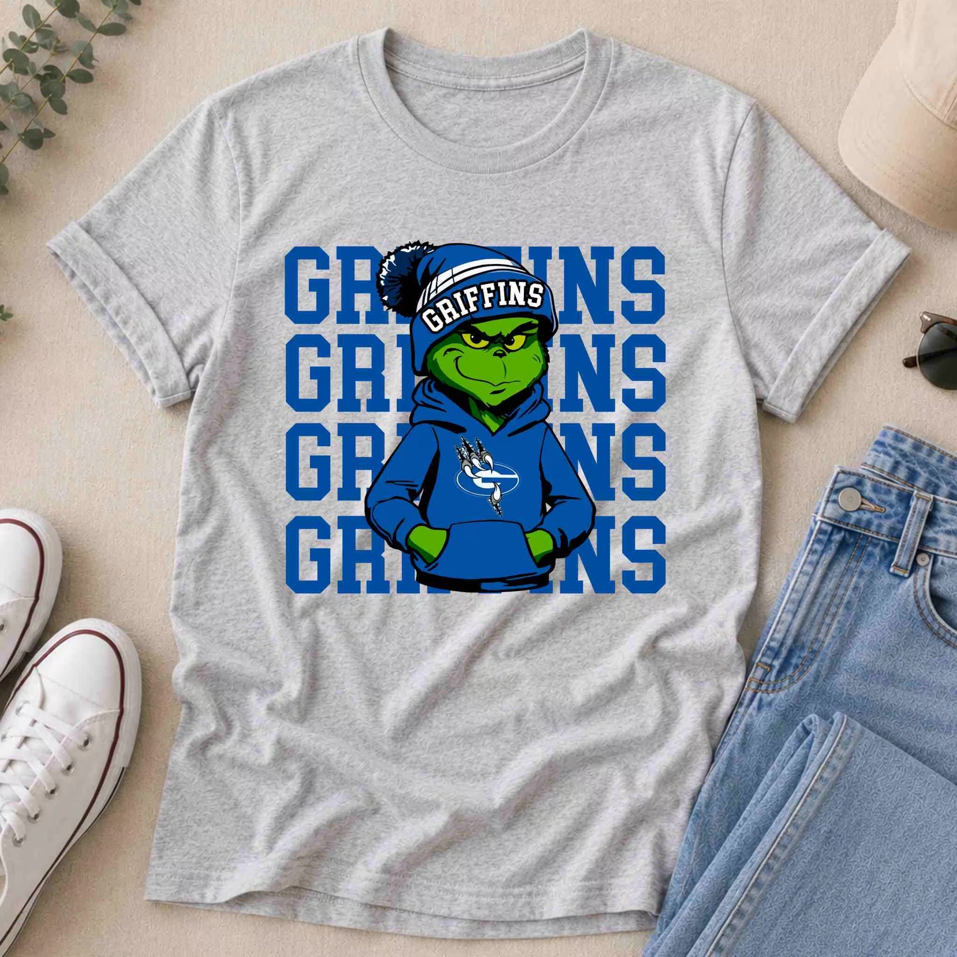 The Griffins Graphic Tee Youth Comfort and School Spirit by Becca's Banging Designs features the Grinch in a blue GRIFFINS hoodie and beanie, with "GRIFFINS" repeated in bold blue—perfect for boosting school pride.