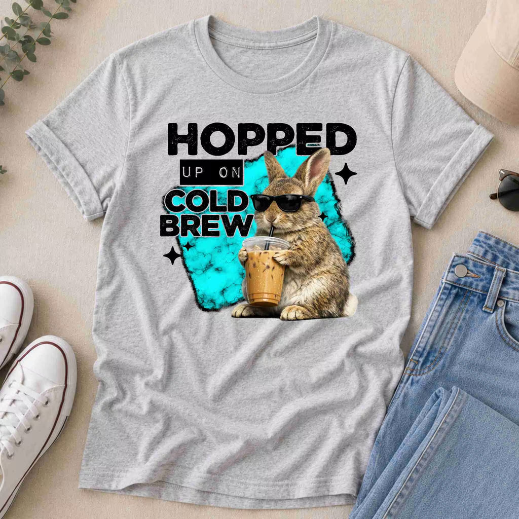 The Hopped Up On Cold Brew Bunny Shirt by Becca's Banging Designs LLC is a gray tee with a cold brew bunny in sunglasses holding iced coffee and "Hopped up on cold brew" text on a blue paint-like background—perfect for unique graphic tee lovers.