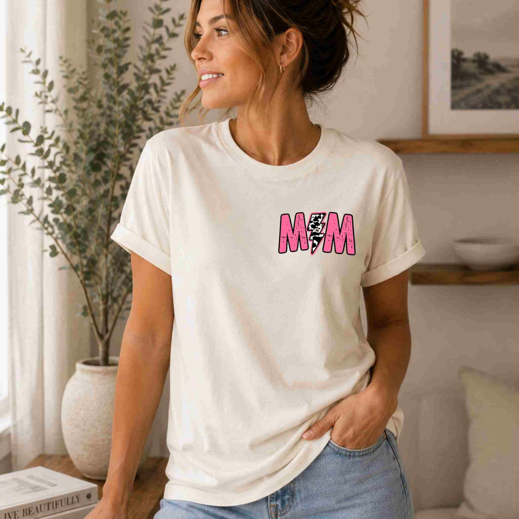 A woman smiles indoors in the Hot Mom Summer Tee by Becca's Banging Designs LLC—a trendy mama graphic shirt with rolled sleeves and “M/M” in pink, perfect for a fresh summer look.