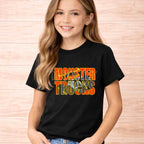 Monster Trucks Kids Shirt Youth Graphic Tee featuring a girl smiling while wearing a black t-shirt with bright orange and yellow letters.