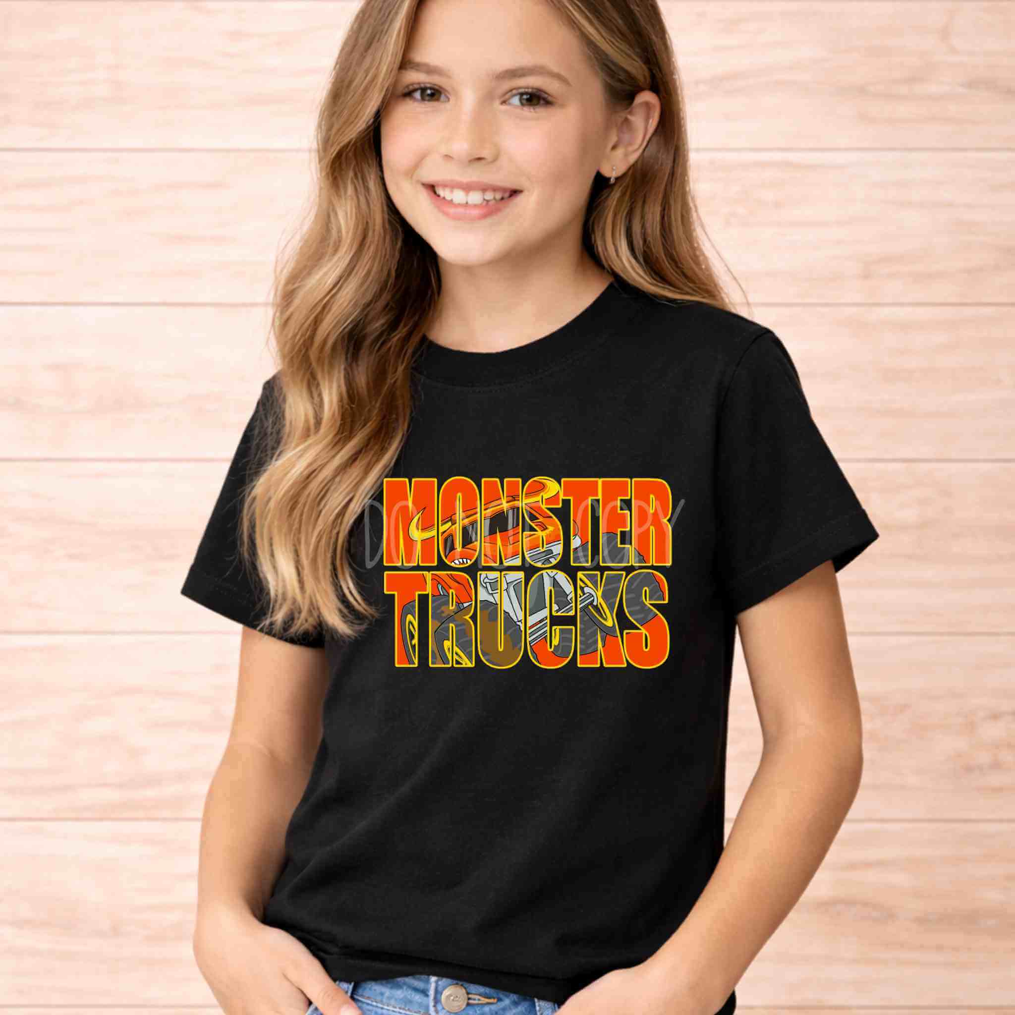Monster Trucks Kids Shirt Youth Graphic Tee featuring a girl smiling while wearing a black t-shirt with bright orange and yellow letters.