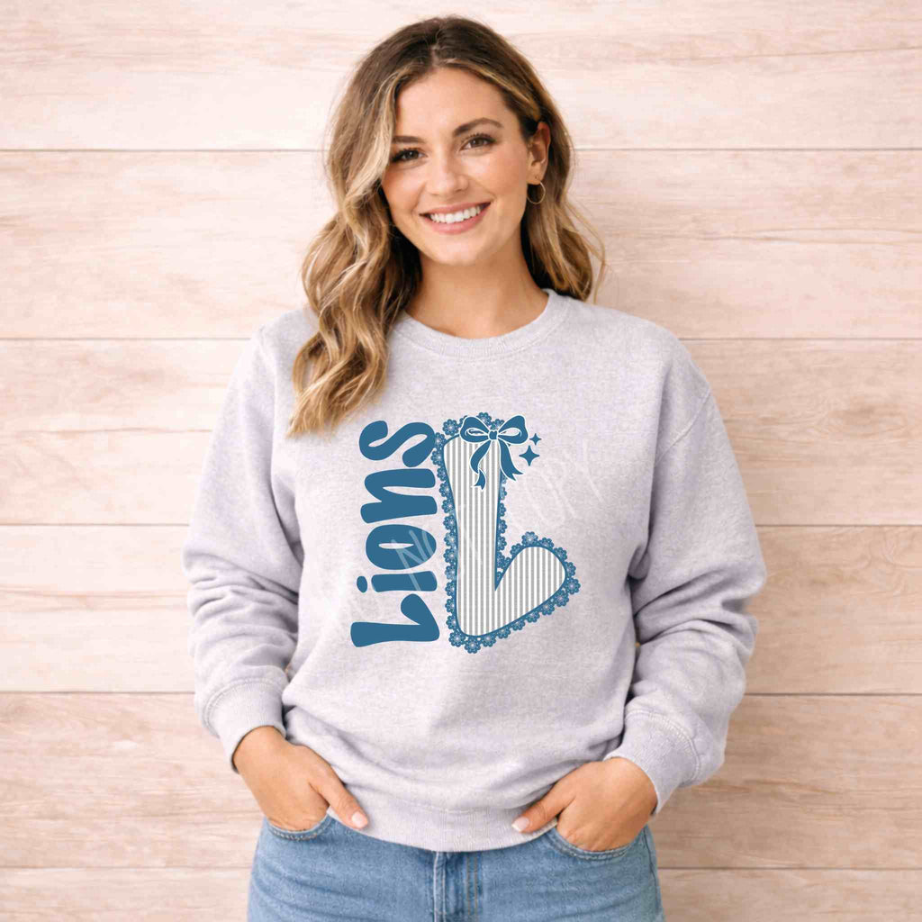 Lions School Spirit Sweatshirt worn by a smiling woman with a bow and varsity 'L' design on a cozy gray crewneck.