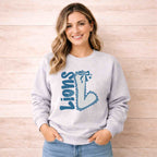 Lions School Spirit Sweatshirt worn by a smiling woman with a bow and varsity 'L' design on a cozy gray crewneck.