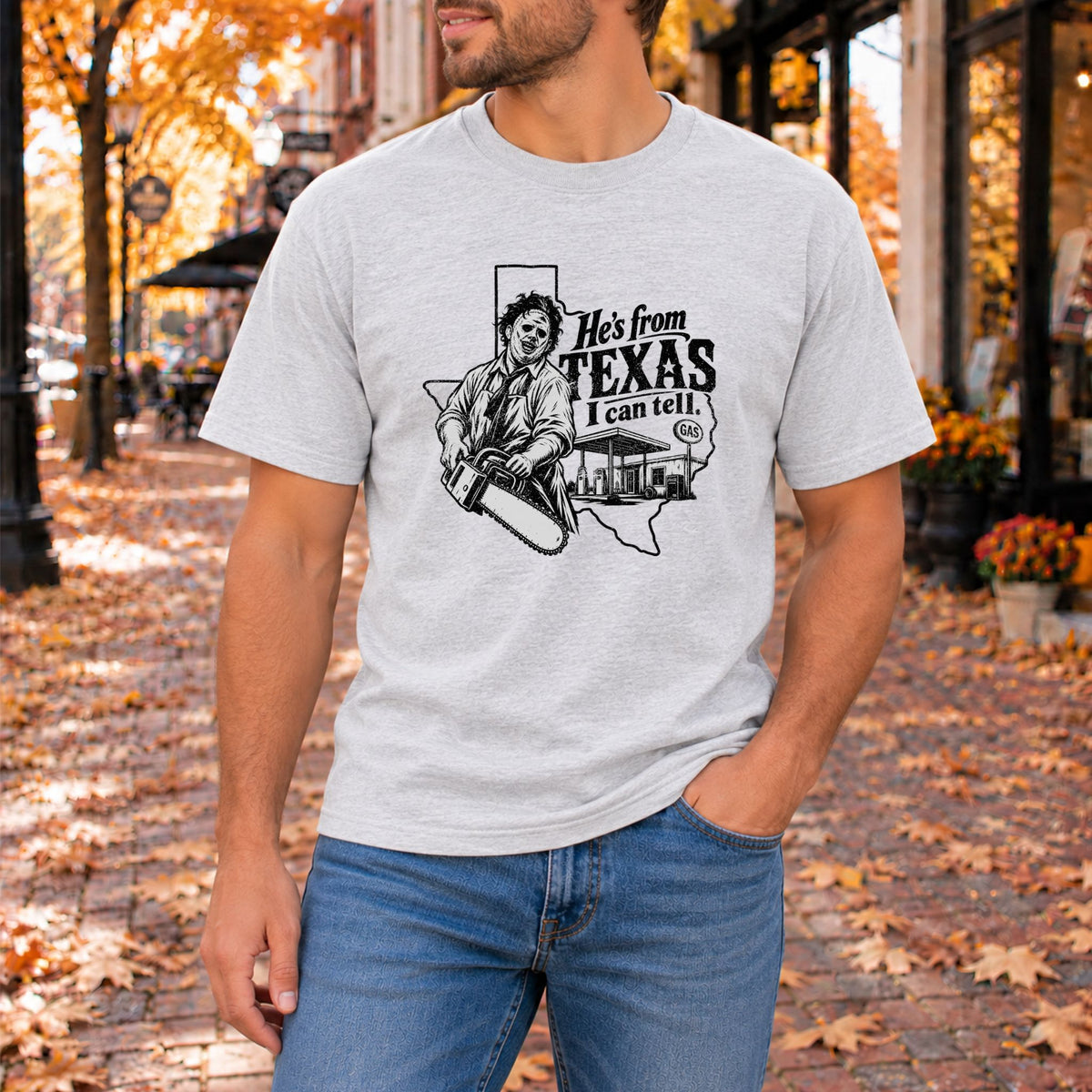Light gray crew-neck horror graphic T-shirt with "He's from TEXAS" text and illustration